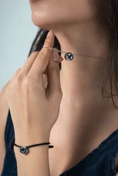 Person wearing a delicate necklace and bracelet with a small round pendant. Story Stroke Travel and Hot air Balloon pendants